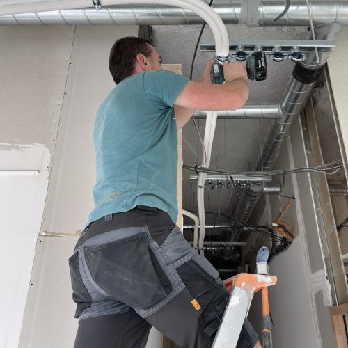 o2lclim-artisan-climatisation-val-de-marne-94-09 Un technicien climatiseur travaillant à l'installation d'un système de climatisation au rez-de-chaussée, outils en main.